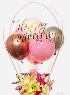 4 small gold silver pink and white balloons inside a Clear balloon printed happy anniversary with White lilies basket